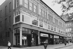 A black and white photo of the building with elaborate but uniform storefront designs. 