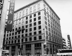 A view of the building in black and white, with large windows and sign prominently on left side with word "Bank" written on it. 