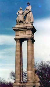 A statue of a set of pillars with some statues on the top and some leafless trees on the bottom. 