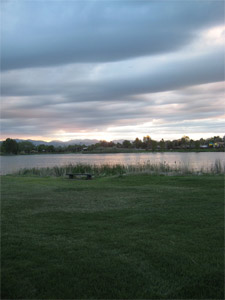 A view of the park with mountains in the background and a series of clouds overhead. In the foreground there is a large area of green grass and the lake behind it. 