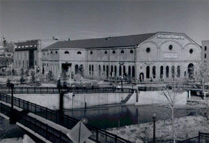 A black and white photo of the building with a bridge on the left and the river in front.
