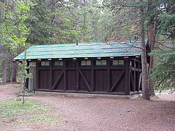 A view of the station with large overhanging gable roof and brown wooden siding surrounded by trees.