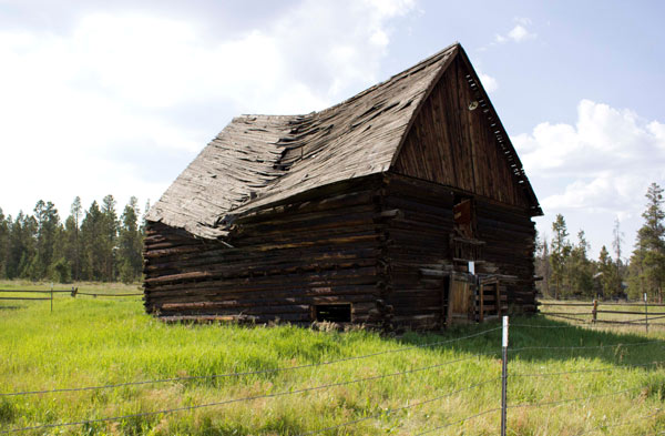 A view of the gable roofed and log walled photo from an angle. Left of center is a large crack down the roof and it is sinking. 
