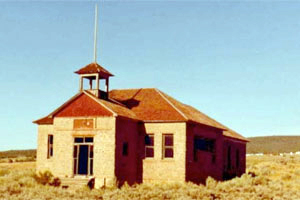 A photo of the school with protruding entrance with gabled roof and bell tower above and hipped roof over main section. 