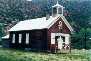 A photo of the schoolhouse from an angle with red walls and white pitched roof and school tower over the center near the entrance on the right.