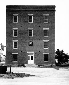A black and white photo of the building with four floors and evenly dispersed windows on the top two and the entrance in the center of the first.