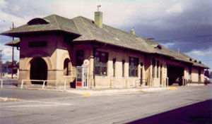 A photo of the depot from an angle with hipped roof and arched entry way on the left. 