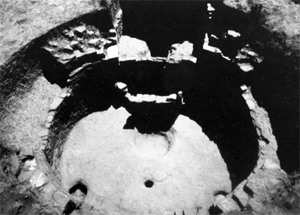A black and white photo of the site with two circular wells, one inside the other. 