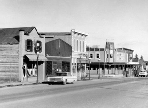 A black and white photo of some buildings in the district with varied fades and a road in front.