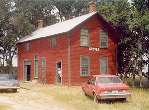 A corner view of the red building with green trim and gabled roof. Two cars are parked in front of the building.