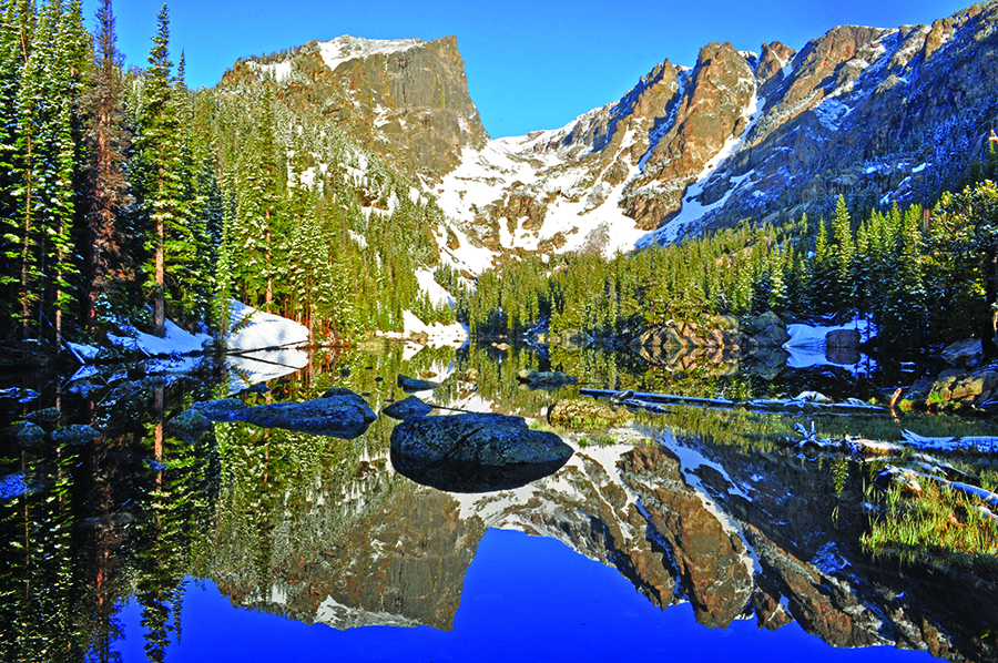 A lake with crystal clear water surrounded by trees and snow capped peaks in Rocky Mountain National Park