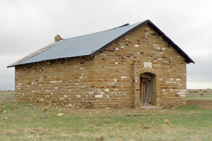 A view of the brick school from an angle with entrance in front and gable roof on top. 