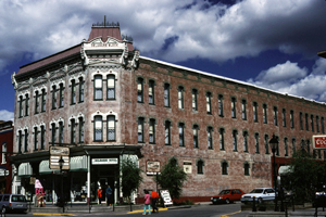 A view of a building in the district with vertical windows over three floors and clipped corner above an awning. 