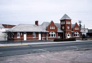 A view of the red-brick depot with gray hipped and gabled roofs and tower in the center.