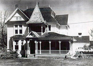 A view of a house in the district with gabled roofs, and covered porch in black and white.