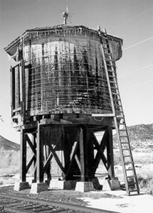 A black and white photo of the round tank with fading paint, and ladder on the right. 