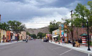 A picture of the district from a street with diagonal parking spaces. On either side of the street are brightly colored buildings and mountain in the background.