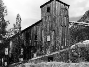 A black and white photo of the wooden mill with gabled roof and slightly lower down on the left is a pitched section. 