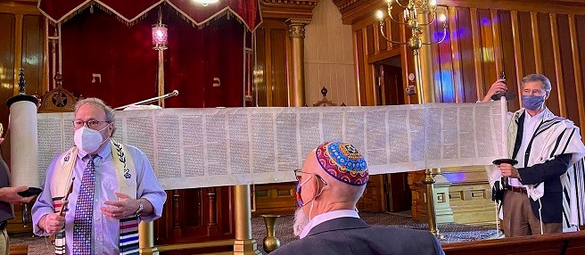 Photo of Rabbi Rob Lennick leading recent Rosh Hashanah services at Temple Aaron. Two men, David London (not pictured, left) and Kim Grant, right, holding each end of the revealed Torah scroll. Ron Rubin, who grew up at Temple Aaron, looks on.