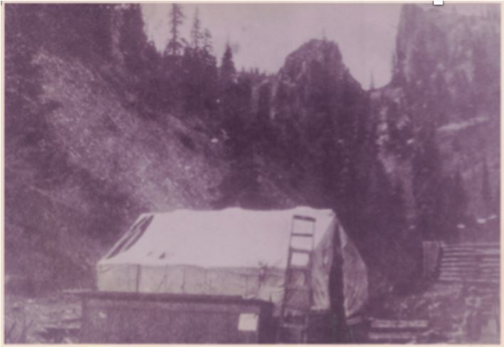 Photo of a large tent erected in a small mountain valley. There is a ladder leaning up against the tent.