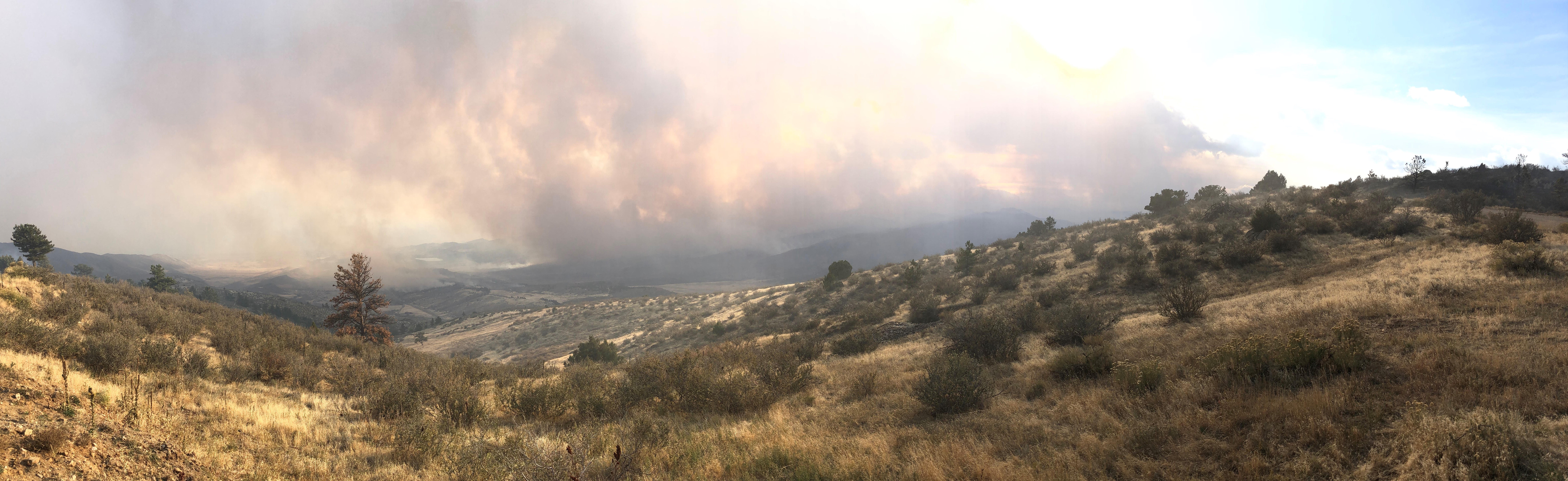 Photo of a wildfire creating huge clouds of dark smoke as it burns the mountain range along the horizon.