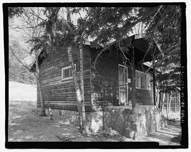 Photo of a small log cabin which sits in the shade of a large pine tree on the McGraw Ranch.