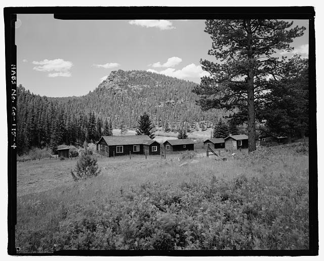 Photo of the McGraw Ranch buildings. In a clearing adjacent to large pine trees, sit three guest cabins and the laundry building, all of one-story log cabin design.