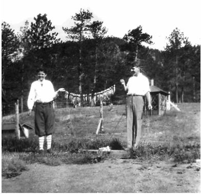Photo of two young men standing a few feet apart, and holding up a string between the two of them. On the string hangs about 20 fish, which the young men have caught fishing that day.