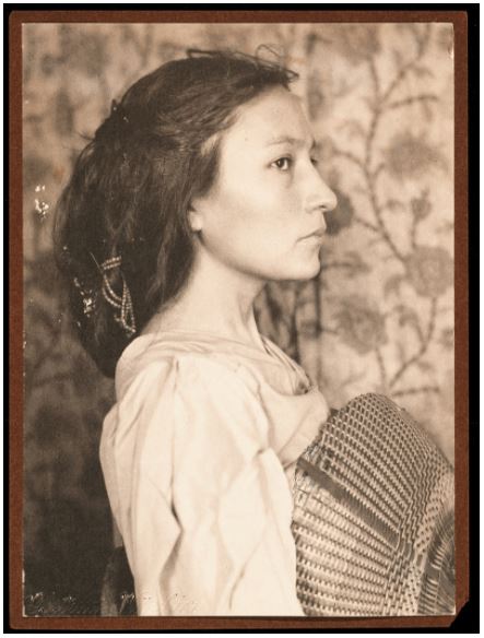 Photographic portriat of an American Indian woman, dressed in both tribal dress and western clothing