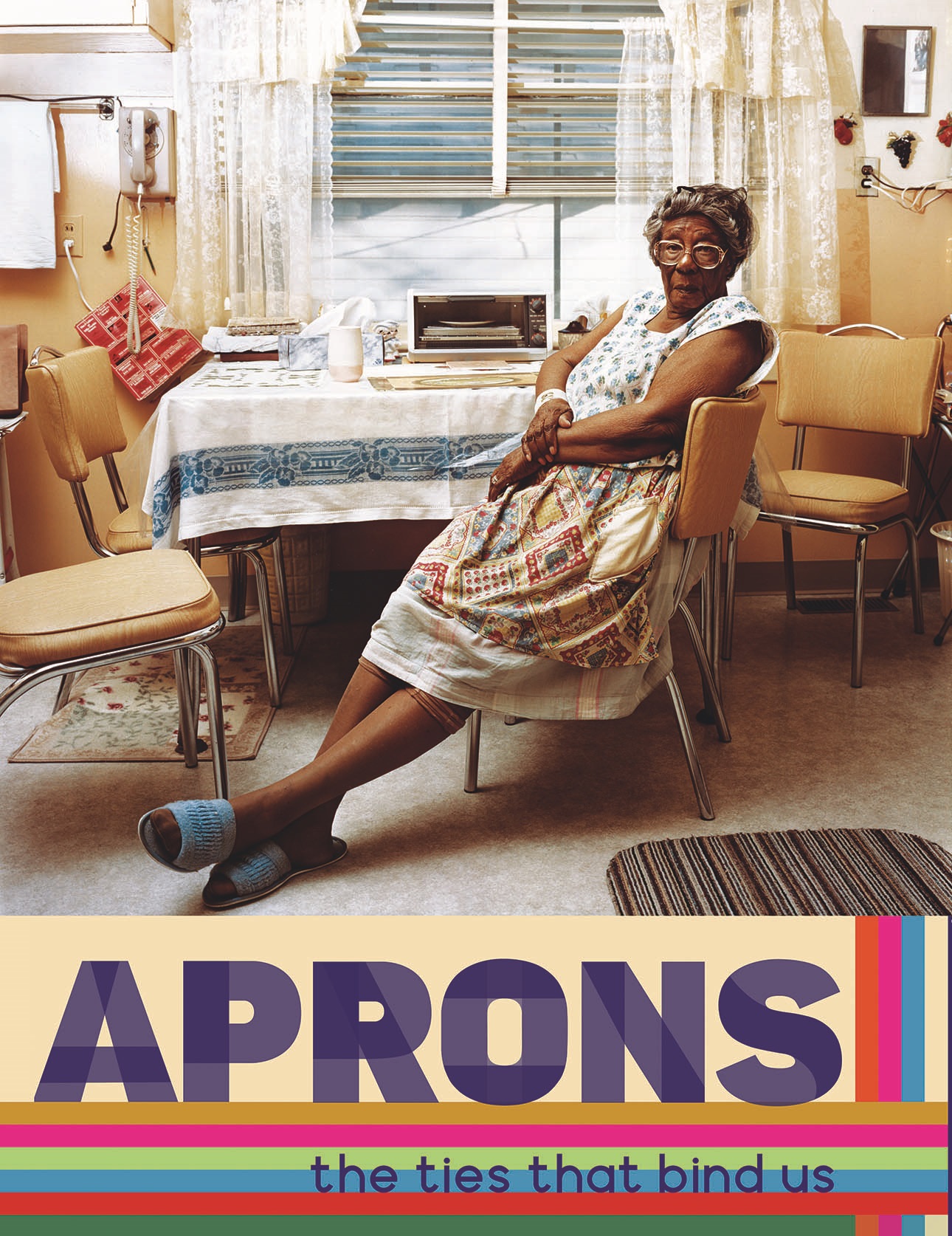 Photo of the banner which hung on the exterior of the History Colorado Center, advertising the Apron Chronicles exhibit. The image shows an older Black woman sitting on a yellow kitchen chair in a yellow kitchen. She is wearing a dress with an apron covering the front, and blue slippers. She is sitting with her arms crossed on her lap and her legs extended in front of her, crossed at the ankles. She is looking at the camera.