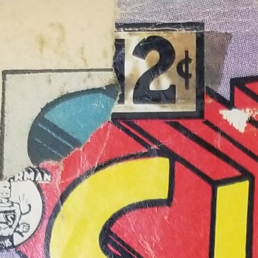 Photo of a fragment from the cover of a comic book. While the title of the comic book is missing (it looks like it may be a cover of Superman, based on the portion of yellow lettering with red block shadows), the price of 12 cents is visible.