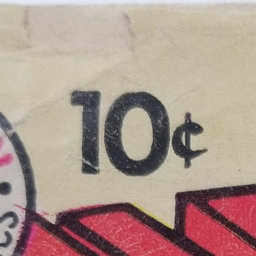 Photo of a fragment from the cover of a comic book. While the title of the comic book is missing, the price of 10 cents is clearly visible, printed in black ink on white paper. A fraction of red ink is directly below the printed price, although its lettering or image is unidentifiable. 