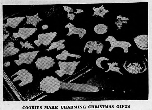 Image of Christmas cookies laid out on a baking sheet. Some of the cookies are decorated with sprinkles or sugar balls, while others are still plain. This image is scanned from a historic newspaper article, and beneath the photo is the title, "Cookies Make Charming Christmas Gifts."