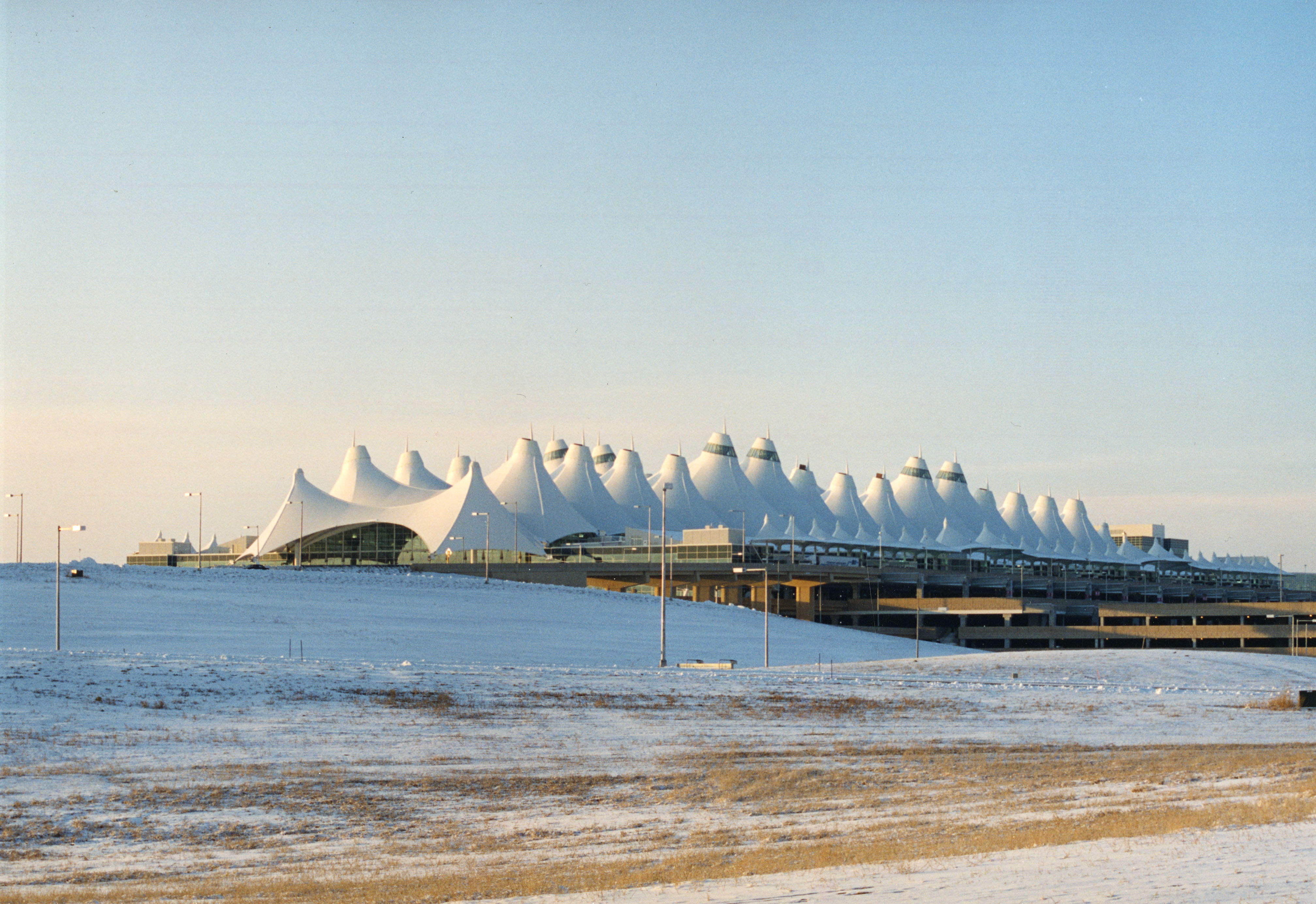 Photo of DIA on a wintry day. There is a thin layer of snow on the ground although the sky is clear and blue. The iconic white tented roof is prominent in this photo.