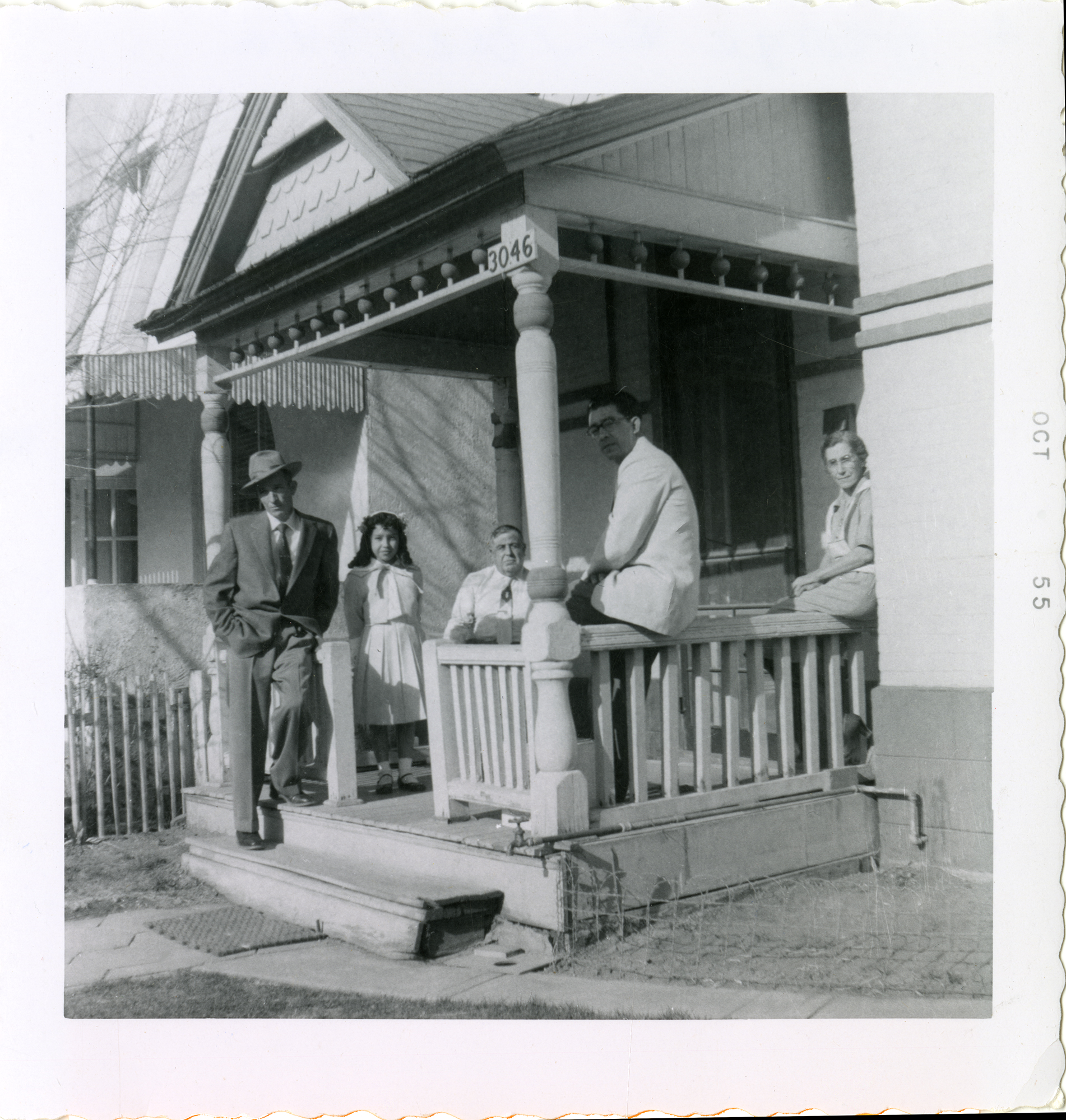 Black and white photograph of members of the Lucero, Trujillo, and Gonzales families sitting and talking on a porch in the Five Points area of Denver, Colorado.