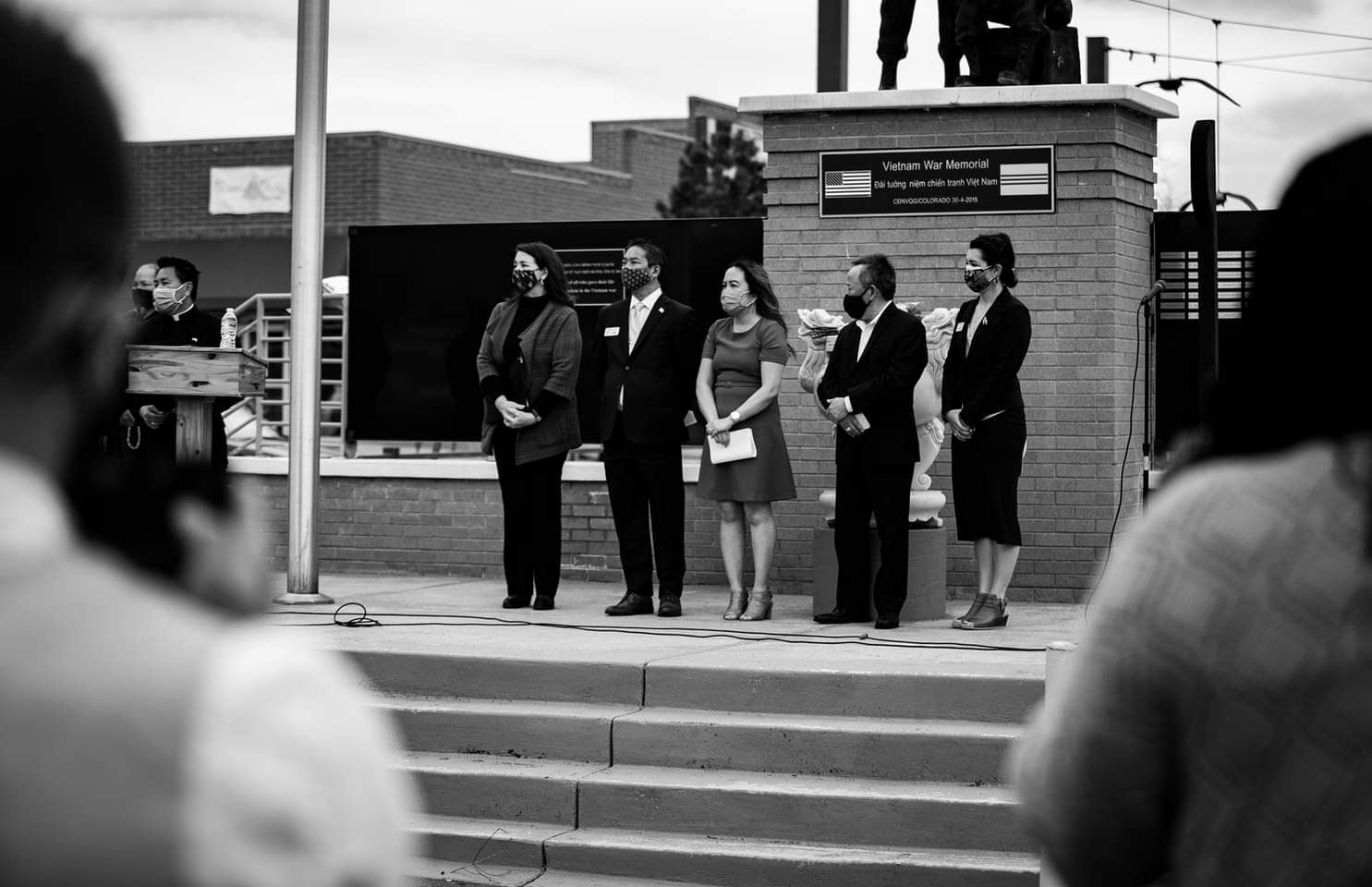 Photo of 4 Asian community leaders including Nga Vương-Sandoval, along with Congresswoman Diana DeGette, attend the AAPI Solidarity Against Racism event at the Việt Nam War Memorial in Denver. They are all standing on a platform, wearing Covid-19 masks facing the speaker at the podium to the left of the image.
