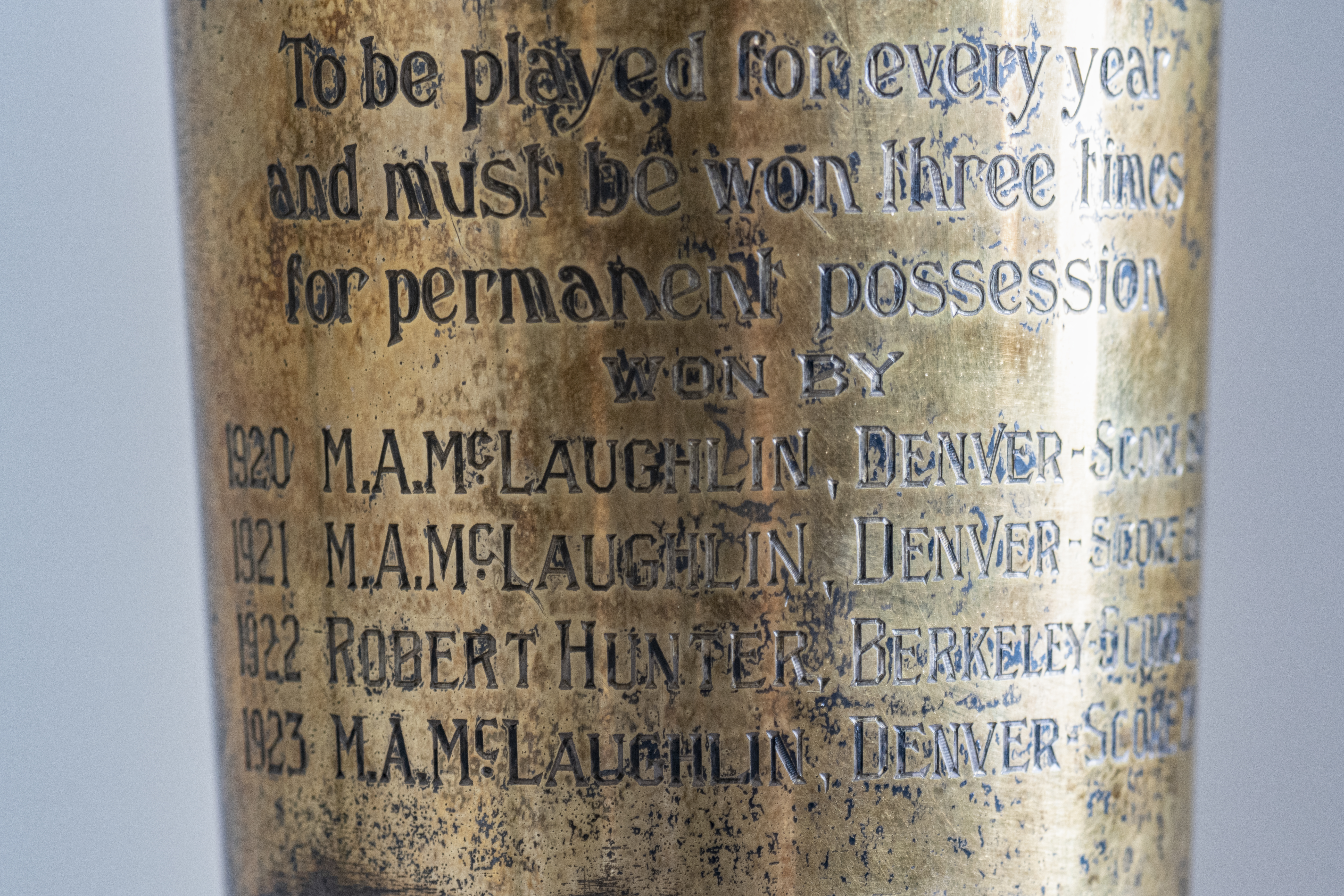 Photo closeup of the inscription on a silver-plated vase that shows some tarnish. The trophy pictured is the original presented to the winner of the Pebble Beach Golf Tournament, which began in 1920. The inscription shows that M.A.McLaughlin won the trophy in 1920, 1921, and 1923. A Robert Hunter won it in 1922.