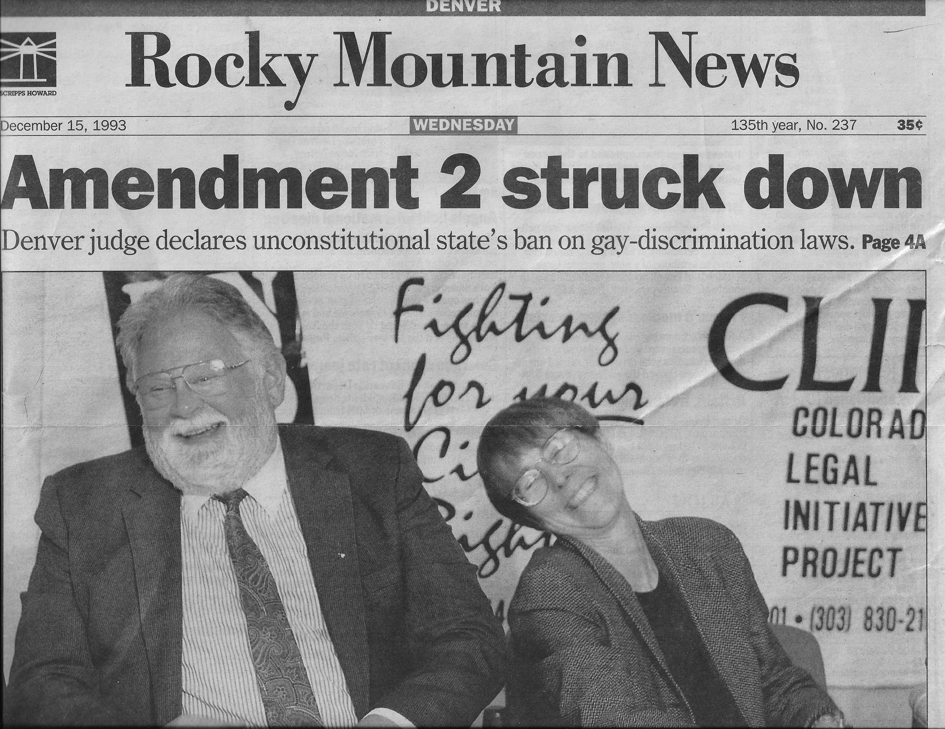 Image of the front page of the Rocky Mountain News newspaper on December 15, 1993. The headline reads "Amendment 2 struck down. Denver judge declares unconstitutional state's ban on gay-discrimination laws. Page 4A" and shows a photo of Jean Dubofsky sitting next to a man, both of them are smiling broadly. 