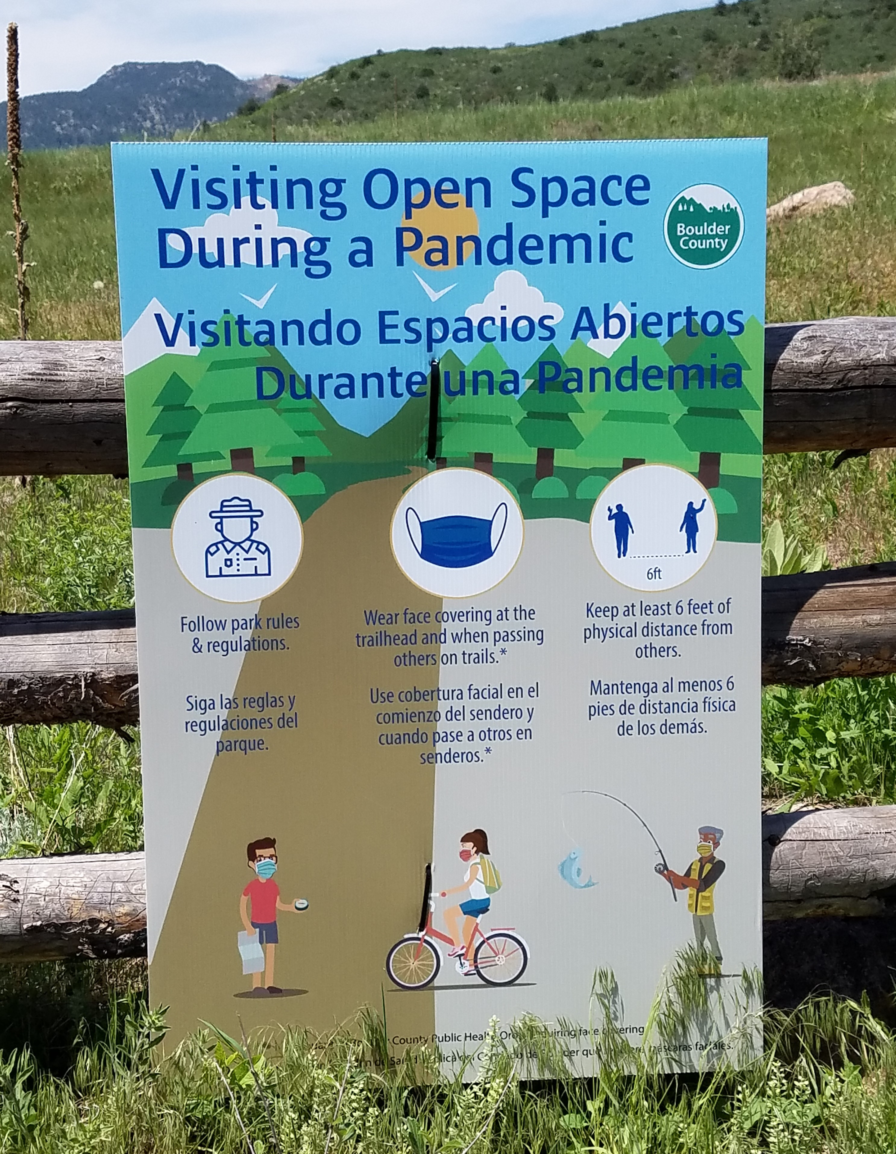 Photo of an outdoor trail sign that says, "Visiting Open Space During a Pandemic." At the bottom of the sign, there are graphics to explain that one must follow park rules, wear appropriate face masks, and keep socially distanced, a minimum of 6 feet from others.