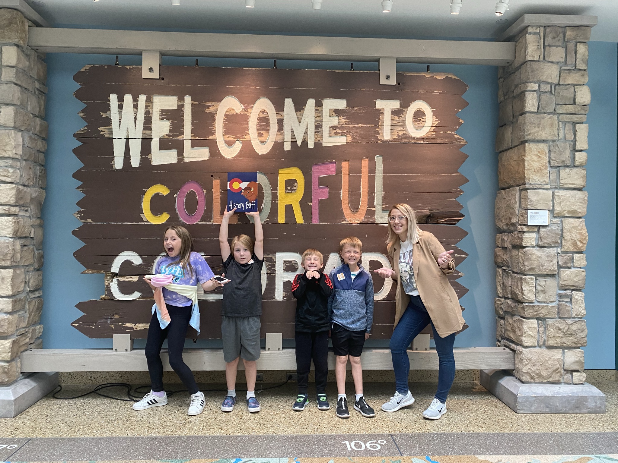 Fourth grade students, all members of the History Buffs membership program for students, pose with their History Buffs packets in front of the Welcome to Colorful Colorado sign at the History Colorado Center.