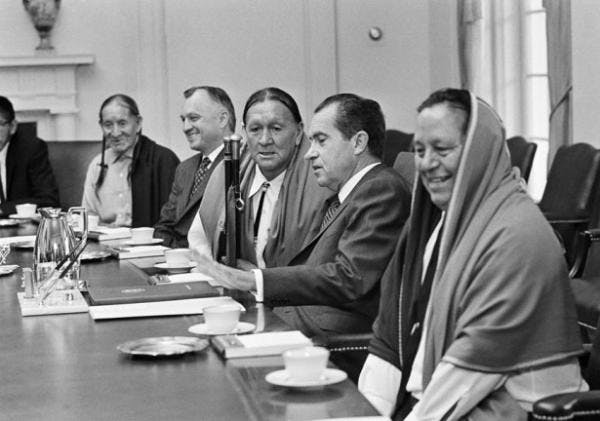 A black and white photograph of President Nixon sitting between tribal leaders during the development of the Self-Determination Act