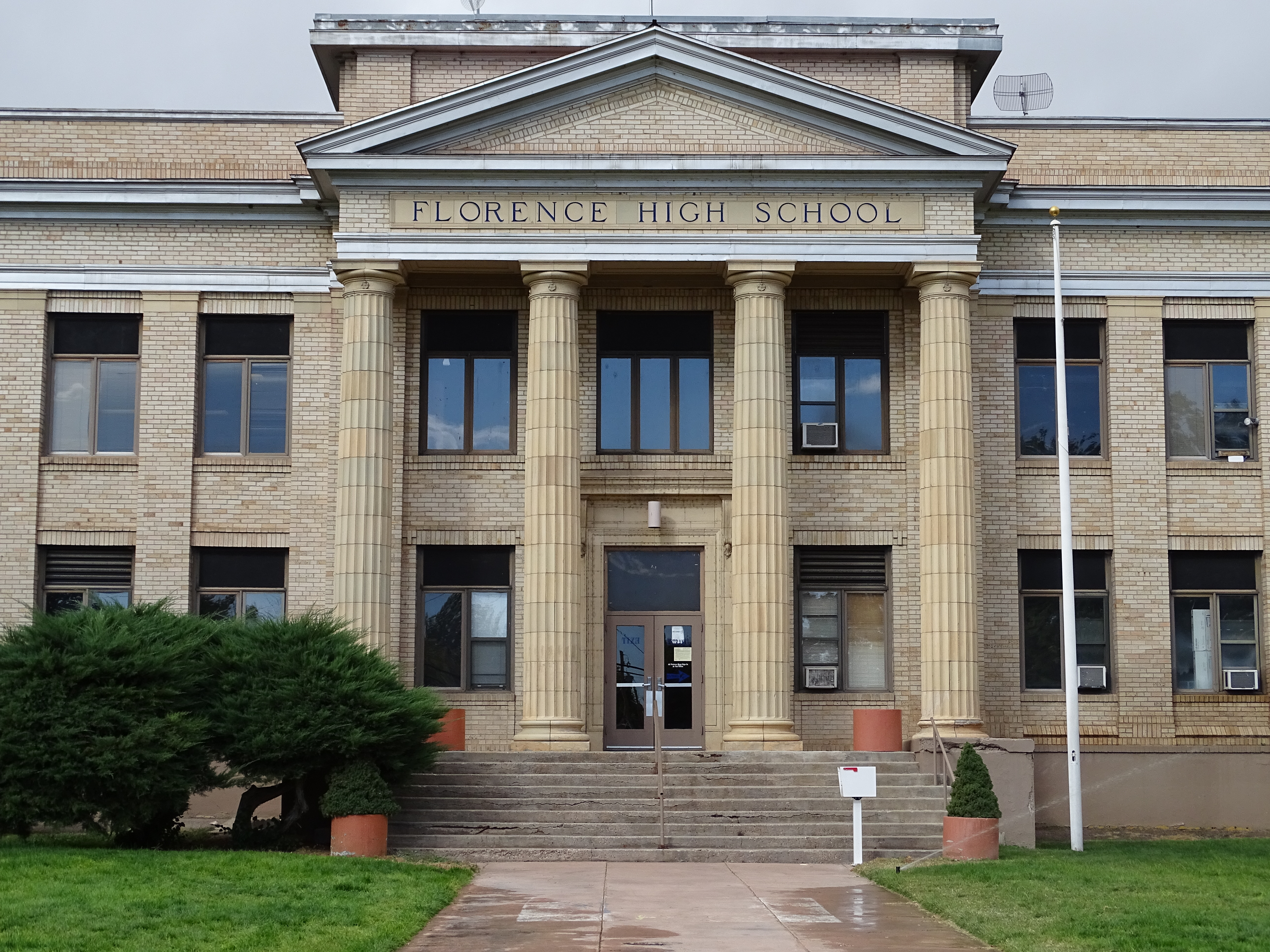 A photo of the front entrance to Florence High School, a blonde brick building with a classical style entablature supported by four large Doric columns.