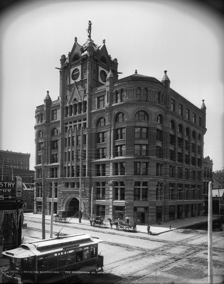 View of the Mining Exchange Building at 15th (Fifteenth) and Arapahoe Streets in Denver, Colorado. Shows a Victorian Romanesque style building with tower, rusticated stone trim and arched doorway. The statue of a miner sits atop the tower. Signs read: "A. W. Rucker Law Office" and "Hicks & Bailey Investment Co." Carriages and wagons are on Arapahoe Street; a sign on a trolley car reads: "Eleventh Ave."