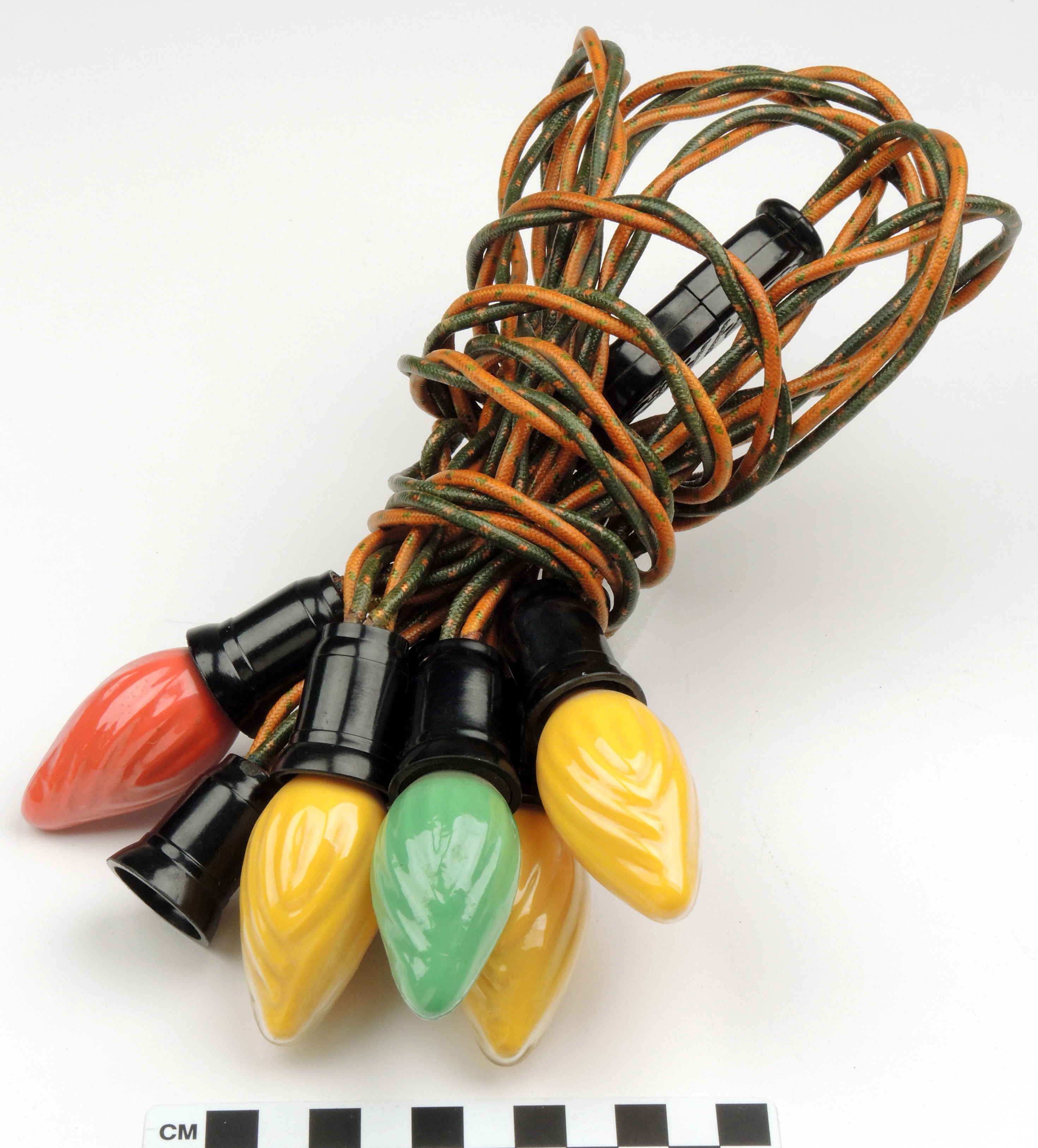 Photo of a string of Christmas lights. The yellow and green cord is gathered into a tidy bundle, with the bulbs at one end. There are five glass bulbs in the shape of a small rounded flame. There are 3 yellow, 1 green, and 1 red bulb in the bunch, with a black plastic base that connects them to the electrical cord.