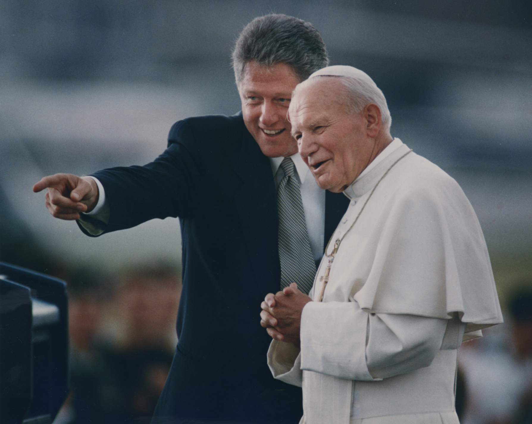 President Bill Clinton and Pope John Paul II stand before a crowd, smiling.