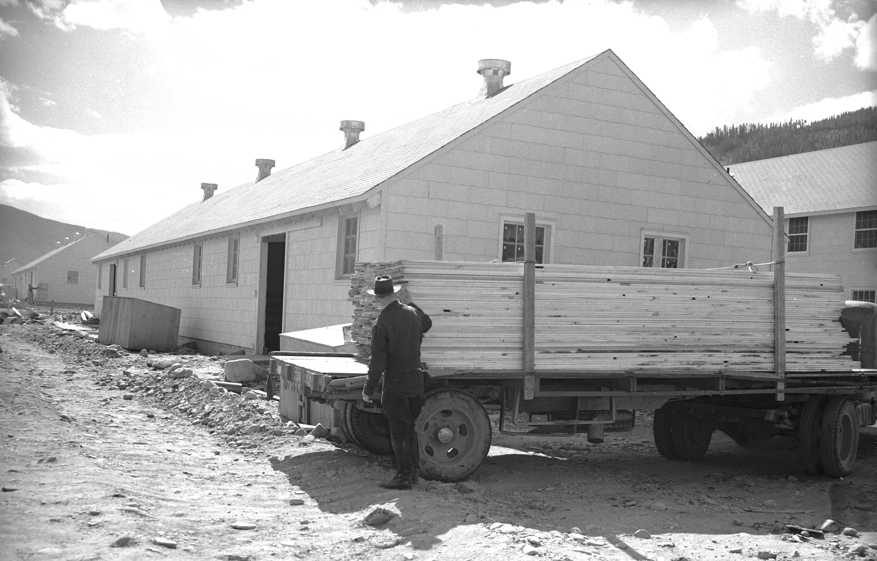 A truck with a load of lumber parked outside a long building.