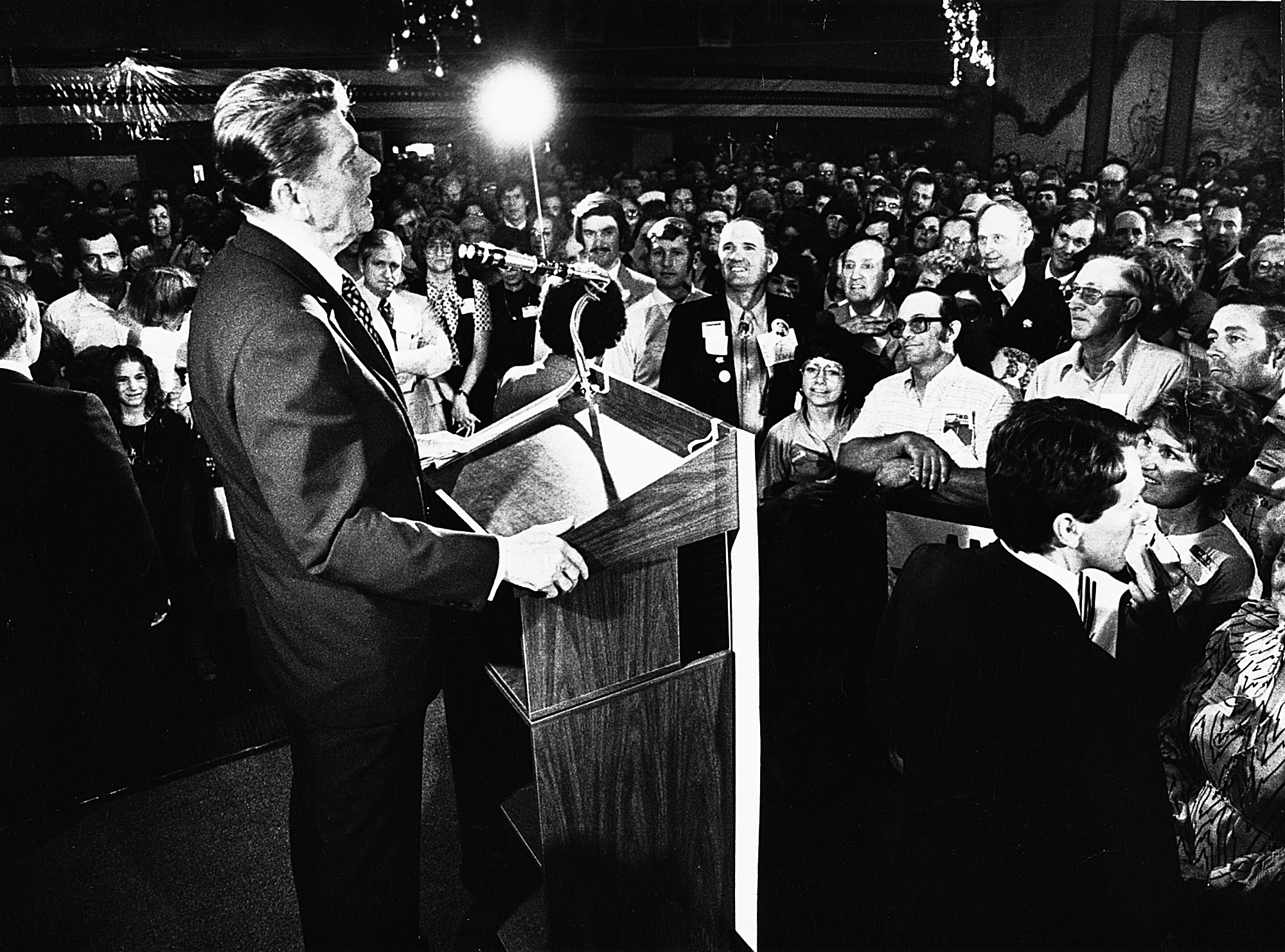 Ronald Reagan standing at a podium in an in-door venue, speaks to a crowd.