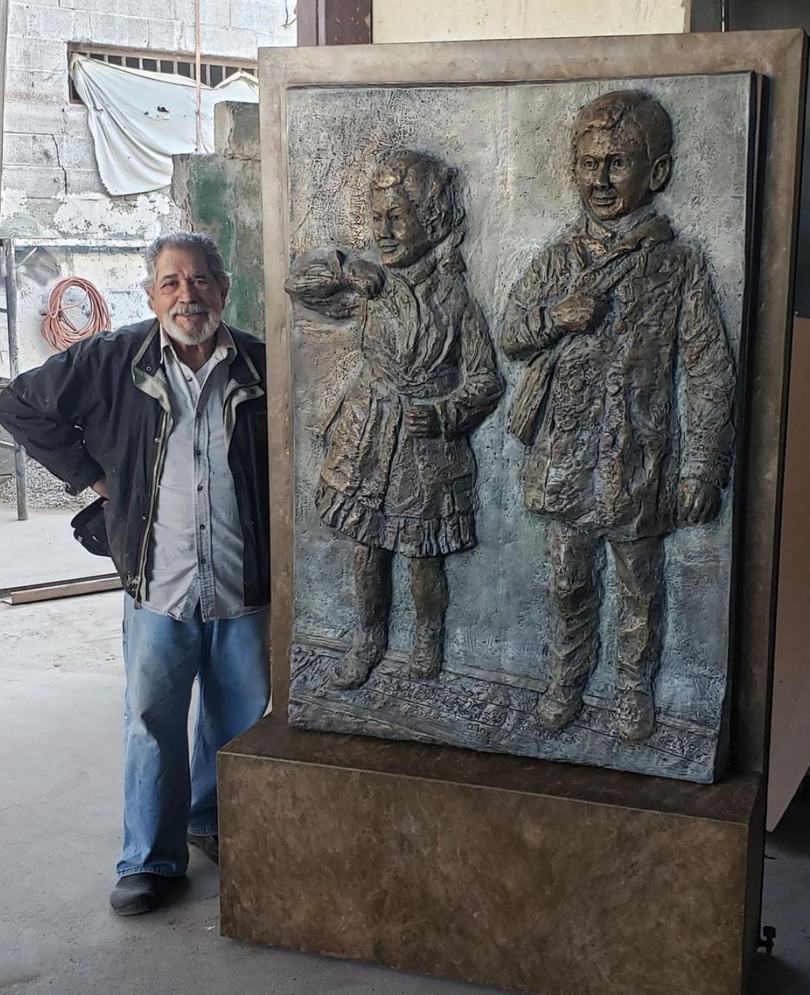 Artist Sonny Rivera with the Maestas sculpture. The sculpture shows two youths, on their way to school, dressed in the clothes of the time period.
