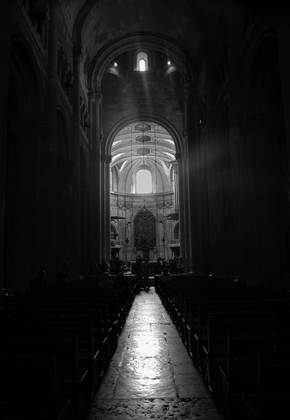 A dark view of a church interior, with pews on either side and the altar straight ahead.