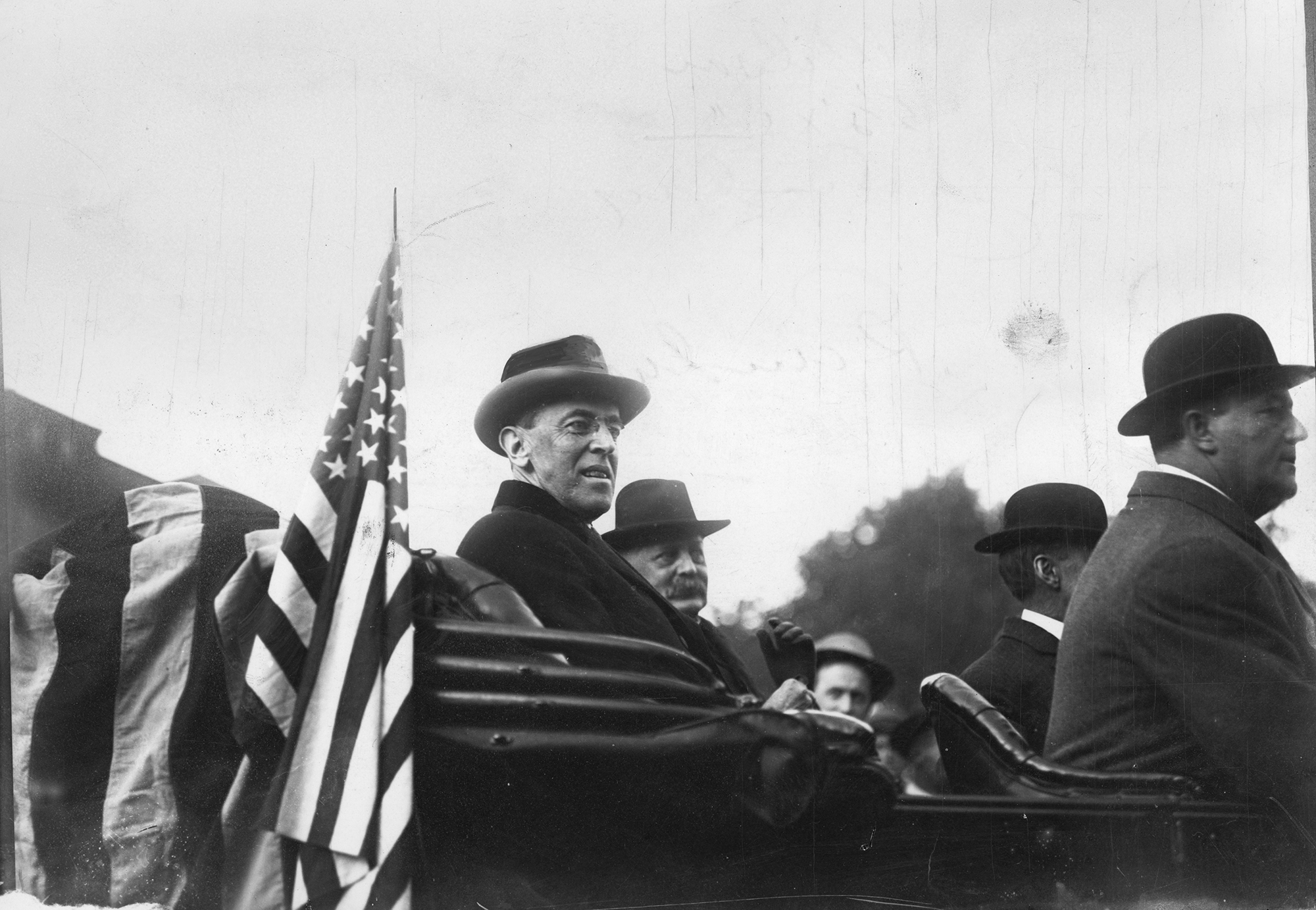 President Woodrow Wilson seated in the back of an open-top automobile with other men.